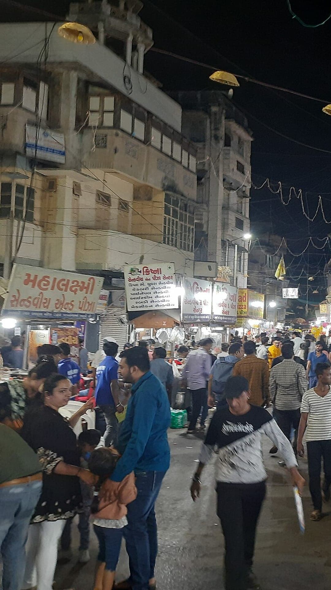 People eating at tables set out in the street at Manek Chowk night market