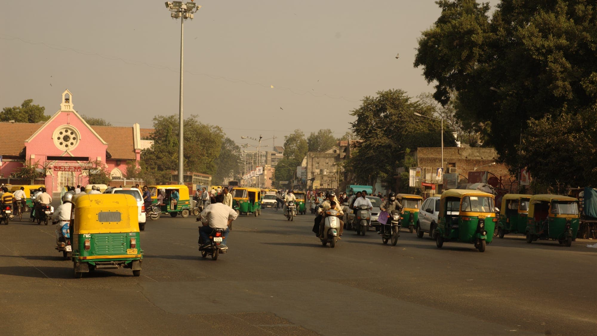 A busy Ahmedabad street with auto-rickshaws and scooters passing shopfronts
