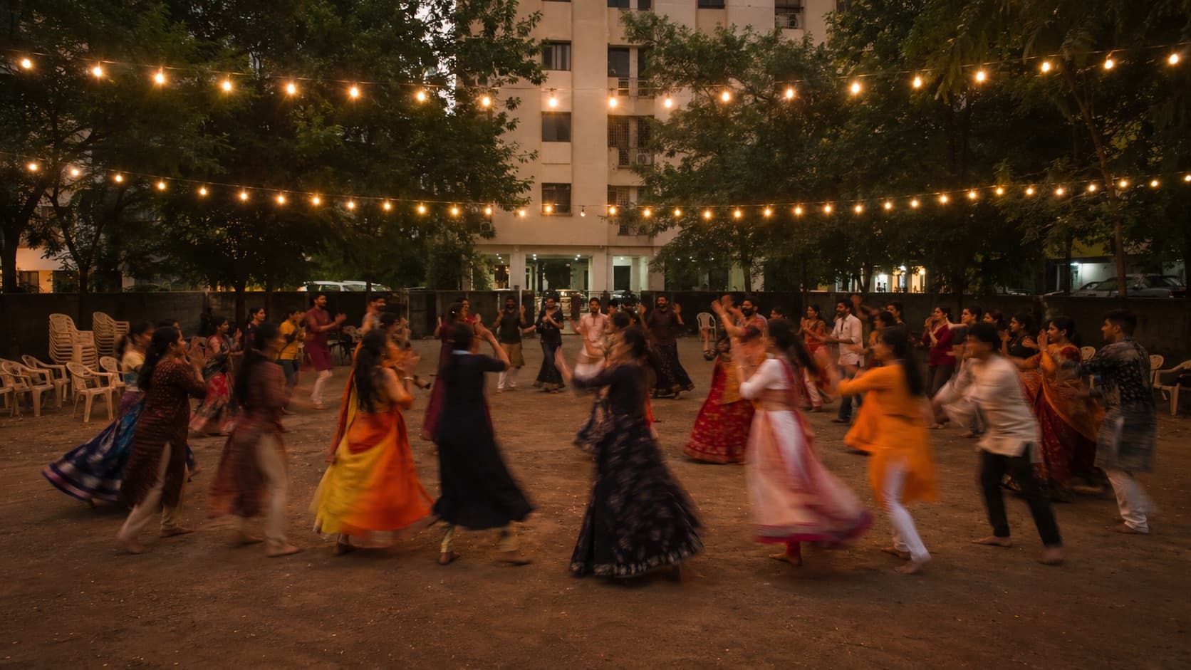 People dancing garba in a circle in a residential society courtyard at dusk, string lights overhead